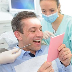 Man in dental chair looking at smile in mirror