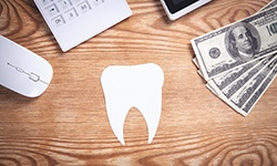 Tooth cutout on table next to money, mouse, and calculator