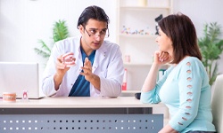 A dentist holds a mouth mold and explains to a female patient how much she can expect her metal-free restoration in Greenfield to cost