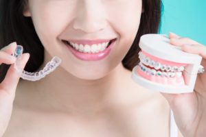 woman with straight teeth holding Invisalign and braces