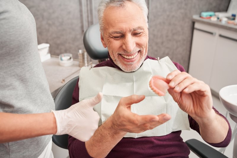 Smiling man holding dentures in his hand while dentist gives thumbs up