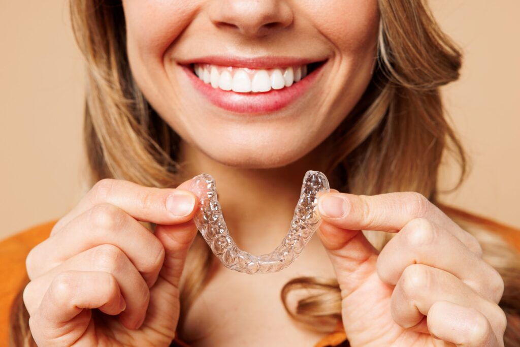 Nose-to-shoulder view of woman smiling holding clear aligner